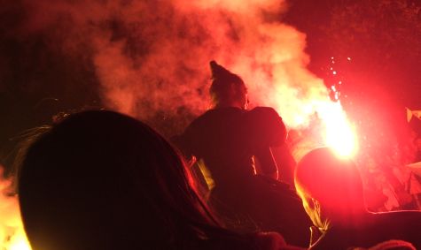 The same woman, against a background of smoke and red fire, stands above the crowd staring.