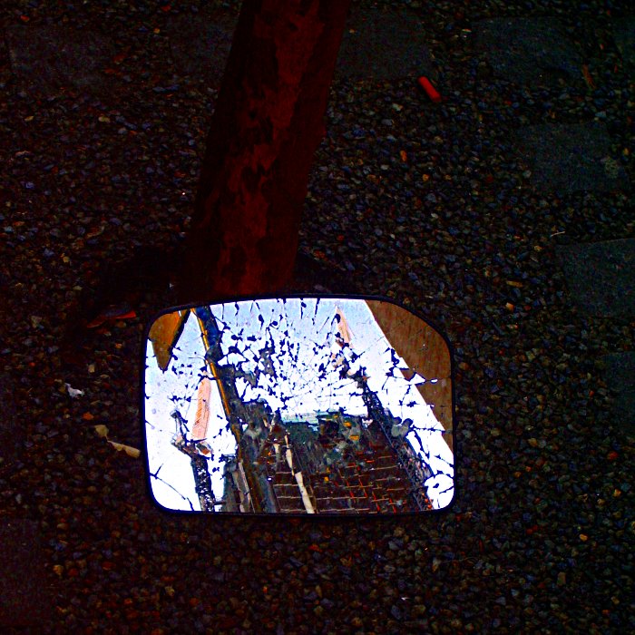 A broken mirror resting against a tree in the middle of a Sydney street reflecting construction that goes on behind the photographer