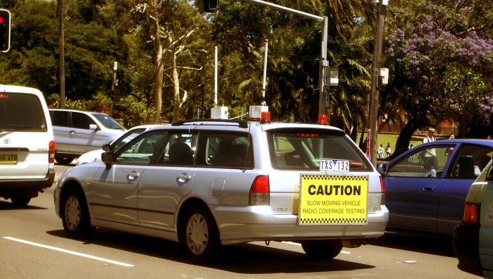 Wardriving in style: a car with a huge antenna on it and a sign.